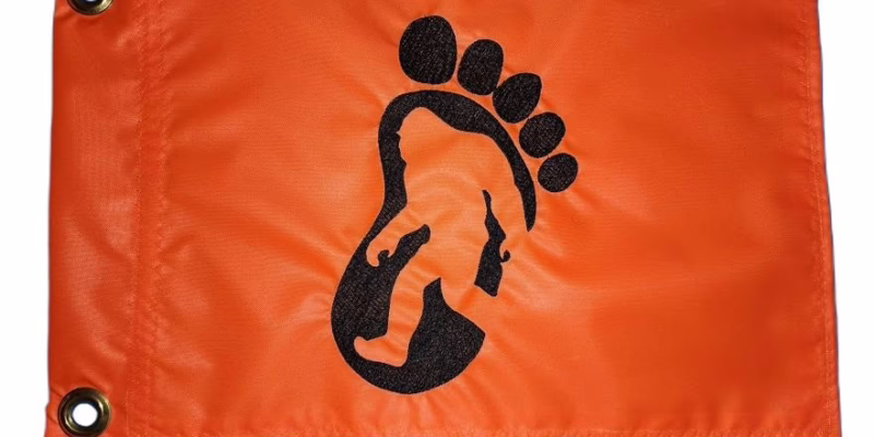 Bigfoot footprint safety flag with embroidered black paw print track and silhouette on bright orange nylon rectangle with brass grommets