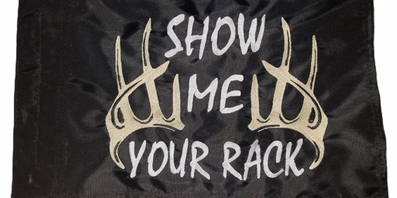 Show Me Your Rack safety flag with dense embroidered white text and tan deer antlers on black nylon rectangle with whip sleeve