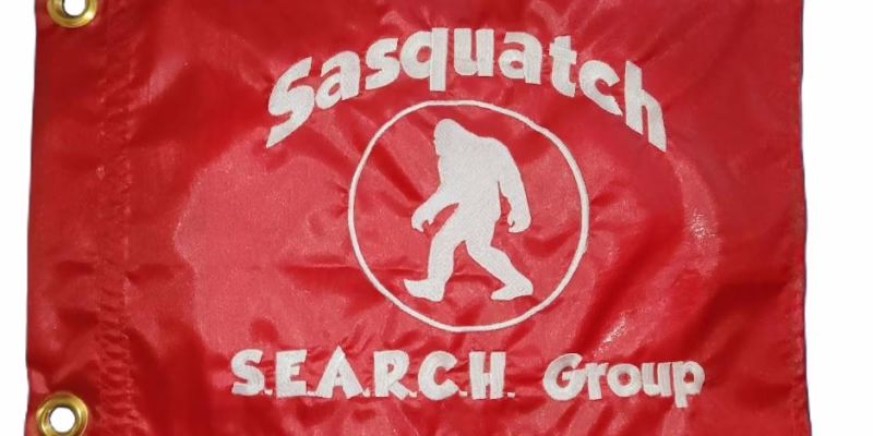 Sasquatch Search Group safety flag with embroidered white circular Bigfoot badge on red nylon rectangle with brass grommets