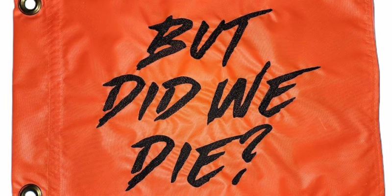 But Did We Die safety flag with black embroidered brush lettering on orange nylon rectangle