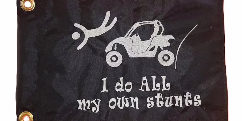 I Do All My Own Stunts UTV safety flag with embroidered flying driver and side-by-side on black nylon rectangle with brass grommets