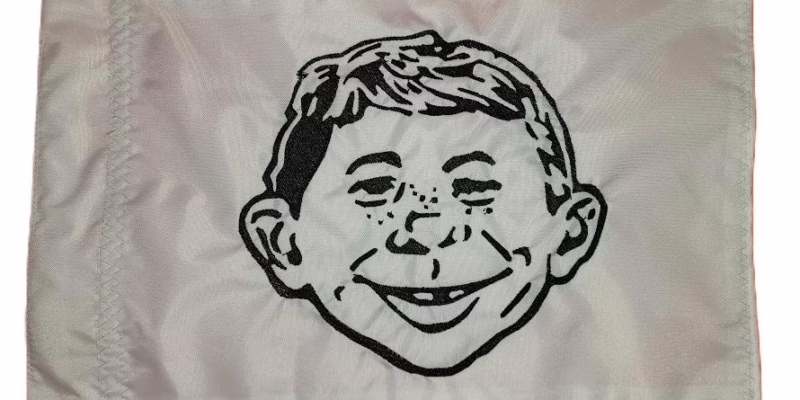 Alfred E. Neuman safety flag with dense embroidered gap-toothed cartoon portrait on nylon rectangle with whip sleeve