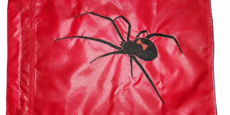 Black Widow spider safety flag with dense embroidered arachnid silhouette and red hourglass on nylon rectangle with whip sleeve