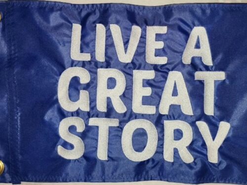 Live A Great Story safety flag with embroidered white stacked block lettering on royal blue nylon rectangle with brass grommets