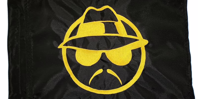 Lowrider Man safety flag with dense embroidered yellow fedora face logo on black nylon rectangle with whip sleeve