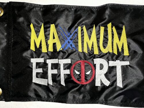 Maximum Effort Deadpool and Wolverine safety flag with dense embroidered yellow and white lettering, blue claw marks, and masked logo on black nylon rectangle with brass grommets
