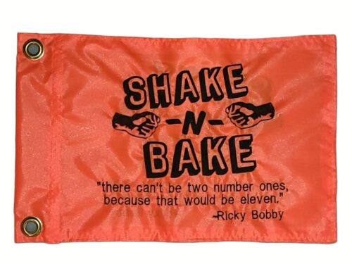 Shake and Bake safety flag with dense embroidered black text, fist bump graphic, and Ricky Bobby quote on orange nylon rectangle with solid brass grommets
