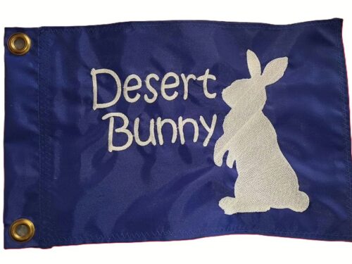 Royal blue rectangle safety flag featuring embroidered white Desert Bunny script lettering and standing cottontail rabbit silhouette with heavy-duty brass mounting grommets
