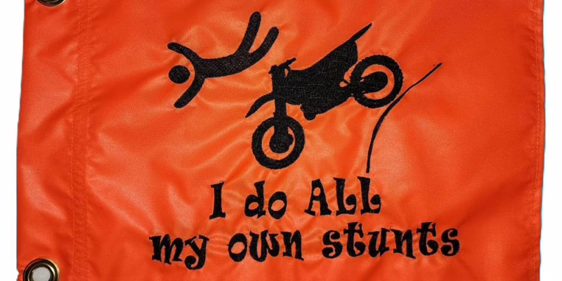 I Do All My Own Stunts dirt bike safety flag with embroidered flying rider and launching motorcycle on bright orange nylon rectangle with brass grommets
