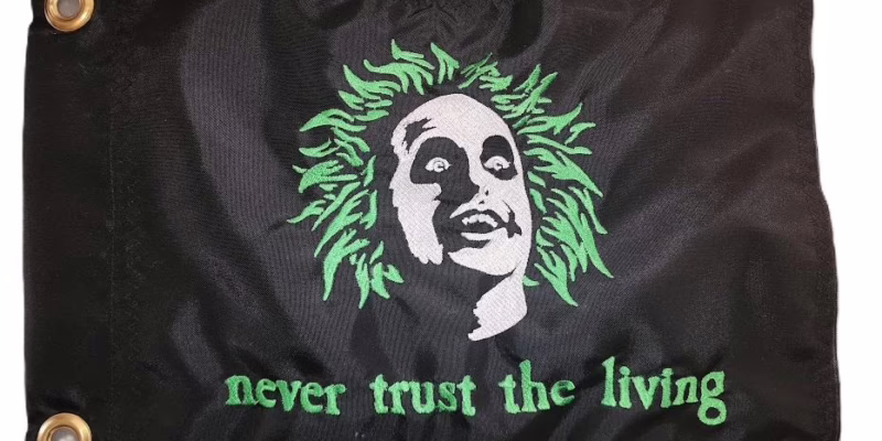 Beetlejuice safety flag with dense embroidered green hair ghost portrait and Never Trust the Living text on nylon rectangle with brass grommets