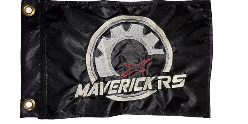 Can-Am Maverick RS safety flag with embroidered silver gear, red X, and Ivory Maverick RS lettering on black nylon rectangle with brass grommets