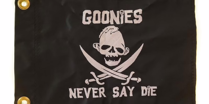 Sloth Never Say Die safety flag with dense embroidered silver skull emblem, crossed cutlasses, and custom movie text on black nylon rectangle with solid brass grommets