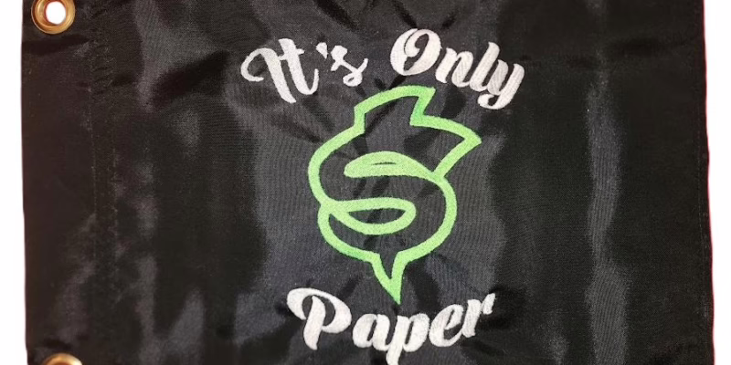 It's Only Paper safety flag with dense embroidered green dollar sign and white text on black nylon rectangle with solid brass grommets