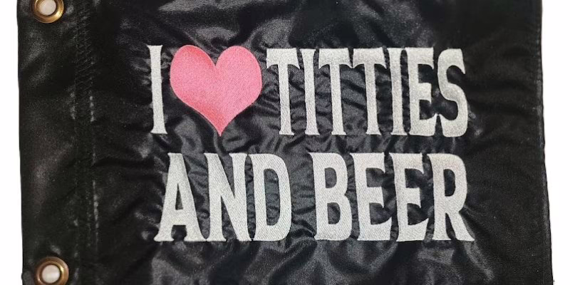 I Heart Titties and Beer safety flag with pink heart and silver embroidered lettering on black nylon rectangle