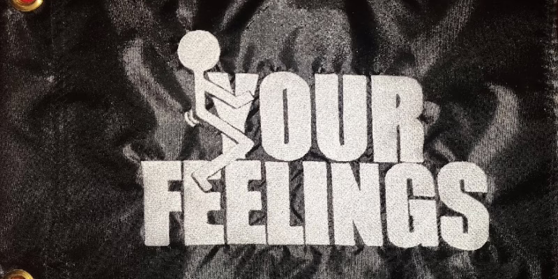 Fuck your feelings safety flag with dense embroidered white text and stick figure graphic on black nylon rectangle with solid brass grommets