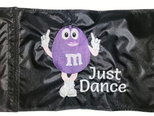 Dancing M&M candy safety flag with dense embroidered mascot and Just Dance text on nylon rectangle with whip sleeve