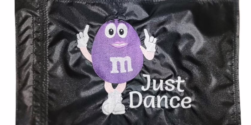 Dancing M&M candy safety flag with dense embroidered mascot and Just Dance text on nylon rectangle with whip sleeve