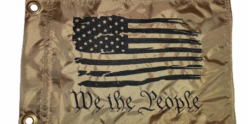 We the People safety flag with dense embroidered black tattered American flag and text on coyote tan nylon rectangle with solid brass grommets