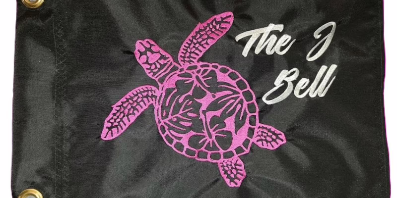 Sea Turtle safety flag with pink embroidered floral honu turtle and white The J Bell script on black nylon rectangle with brass grommets