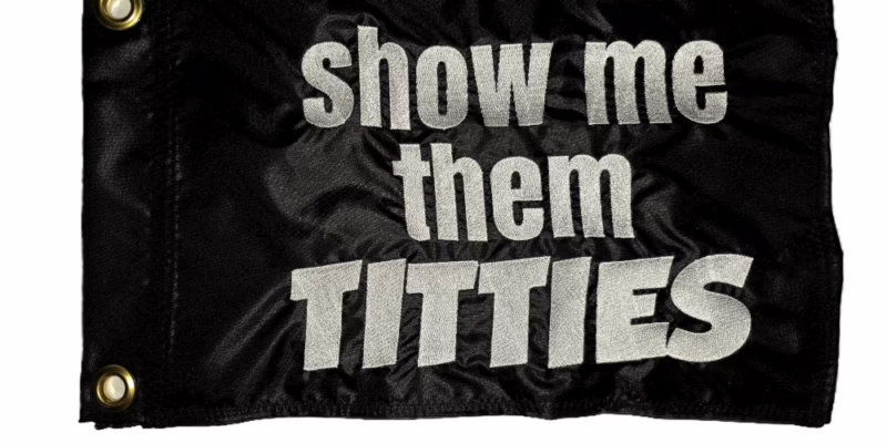 Show Me Them Titties safety flag with silver embroidered block lettering on black nylon rectangle